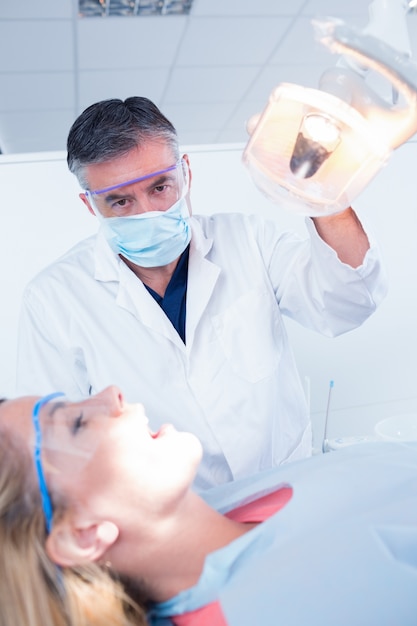 Dentista che esamina i denti dei pazienti in sedia sotto luce intensa