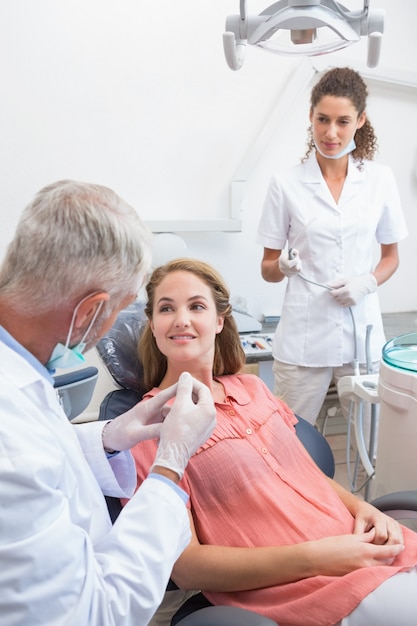 Dentista che esamina i denti dei pazienti nella sedia dei dentisti con l&#39;assistente