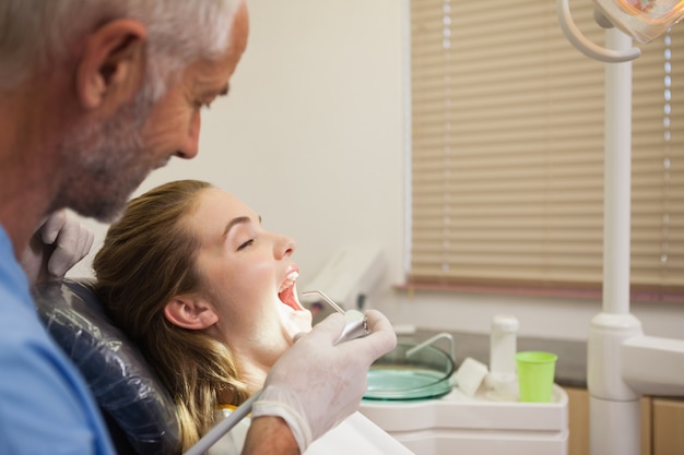 Dentista che esamina i denti dei pazienti nella sedia dei dentisti sotto luce intensa