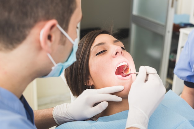 Dentista che esamina i denti del paziente con uno specchio della bocca