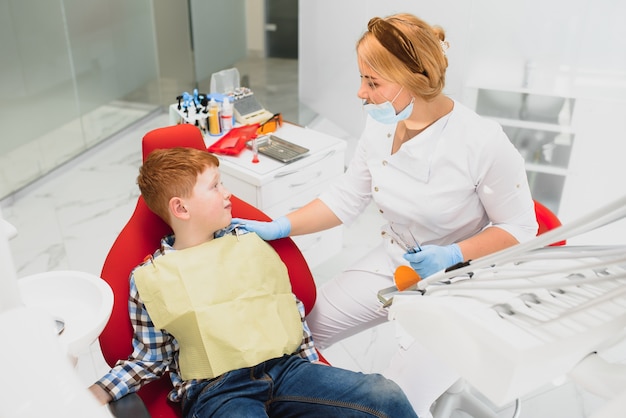 Dentista che indossa la maschera. Dentista bambino dai capelli rossi che indossa la maschera esaminando ragazzo carino