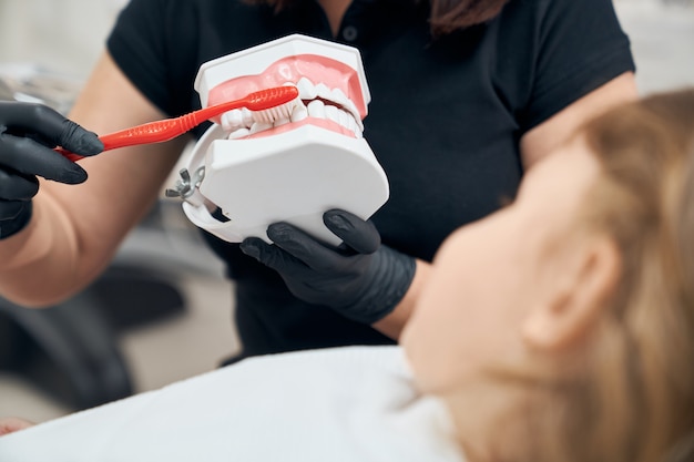 Dentista che mostra a ragazza come spazzolare i denti.