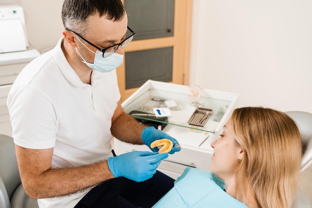 Dentista che mostra il calco dei denti della paziente prima dell'impianto dentale Procedura di creazione di corone e allineatori di protesi dentarie