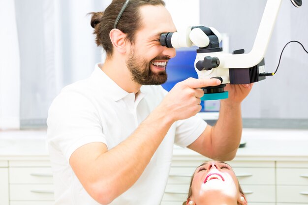 Dentista che per mezzo del microscopio controlla i denti del paziente