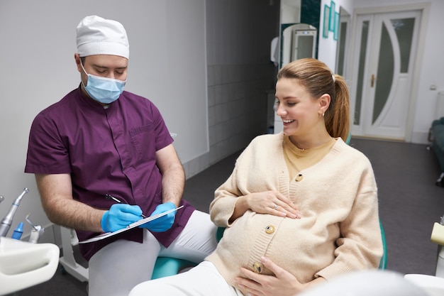 Dentista che prescrive il trattamento dopo l'esame della cavità orale della donna incinta nello studio dentistico