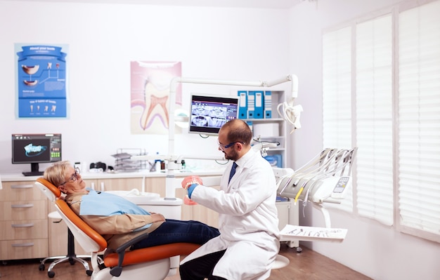 Dentista che spiega l'igiene orale tenendo il modello di cavità durante la consultazione della donna anziana. Cura dei denti medici che discute con una donna anziana sull'igiene della bocca.