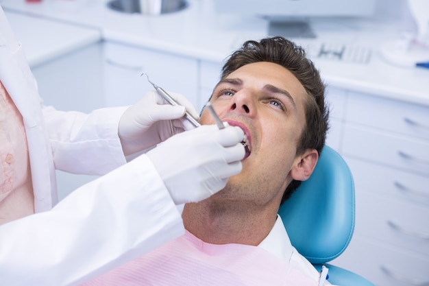 Dentista che tiene attrezzatura medica mentre dà trattamento all'uomo