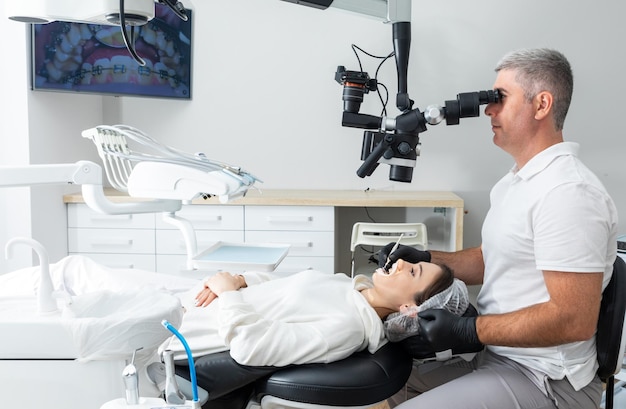 Dentista che utilizza il microscopio dentale che tratta i denti del paziente presso l'odontoiatria della medicina dell'ufficio della clinica dentale