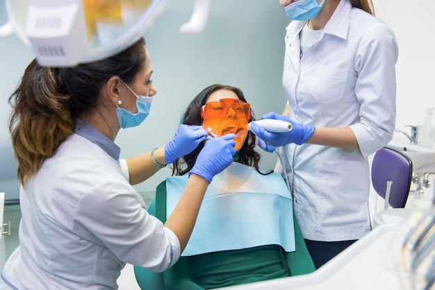 Dentista che utilizza la lampada fotopolimerizzatrice Due stomatologi con un paziente