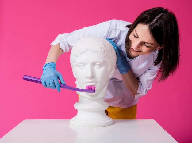 Dentista della donna che lava i denti di una statua antica usando un grande spazzolino da denti