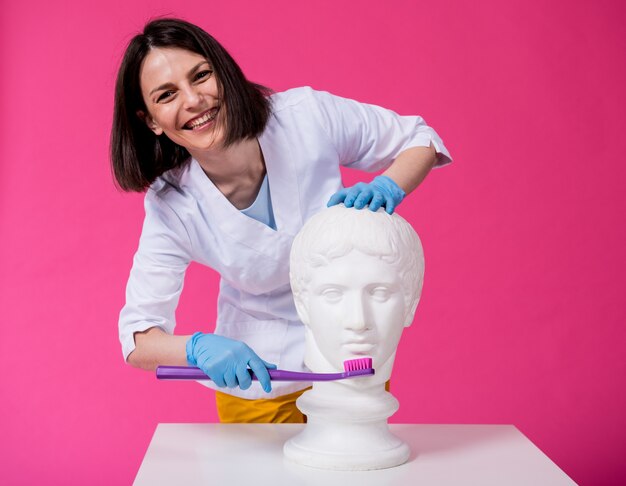 Dentista della donna che lava i denti di una statua antica usando un grande spazzolino da denti