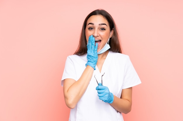Dentista della donna che tiene gli strumenti isolati sulla parete rosa con l'espressione facciale di sorpresa
