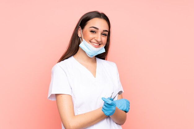 Dentista della donna che tiene gli strumenti isolati sulla risata rosa della parete