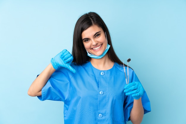 Dentista della giovane donna che tiene gli strumenti sopra l'azzurro isolato orgoglioso e soddisfatto di sé