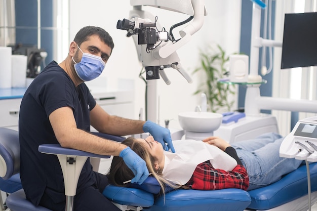 Dentista di successo in maschera medica seduto vicino al paziente sulla sedia guardando a porte chiuse