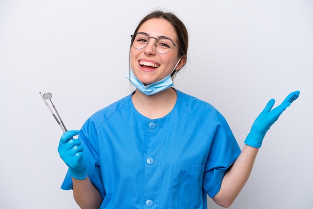 Dentista donna caucasica che tiene gli strumenti isolati su sfondo bianco con espressione facciale scioccata