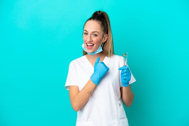 Dentista donna caucasica che tiene strumenti isolati su sfondo blu che celebra una vittoria