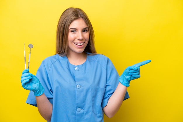 Dentista donna caucasica che tiene strumenti isolati su sfondo giallo che punta il dito di lato