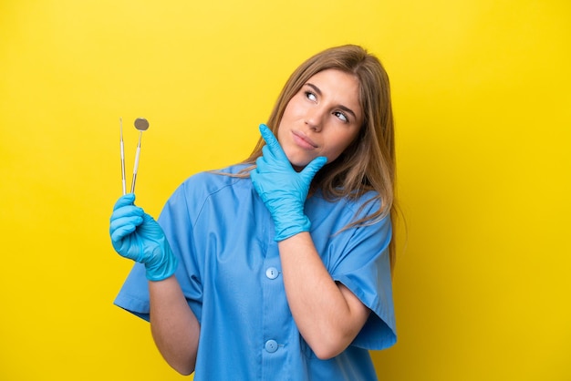 Dentista donna caucasica che tiene strumenti isolati su sfondo giallo con dubbi