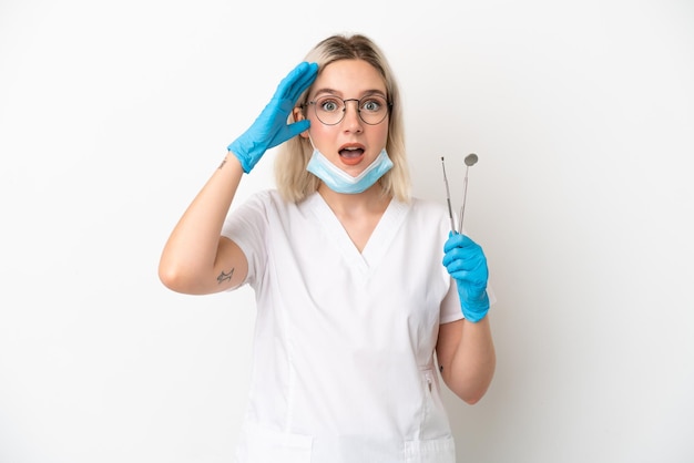 Dentista donna caucasica tenendo gli strumenti isolati su sfondo bianco con espressione di sorpresa