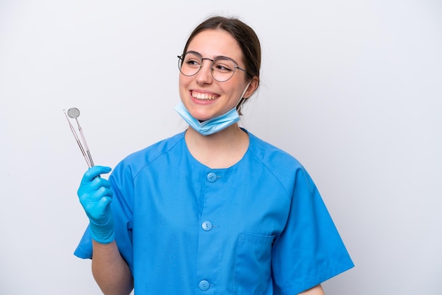 Dentista donna caucasica tenendo gli strumenti isolati su sfondo bianco guardando di lato e sorridente