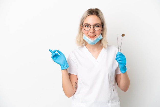 Dentista donna caucasica tenendo gli strumenti isolati su sfondo bianco puntando il dito sul lato