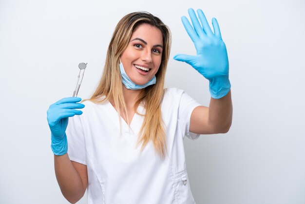 Dentista donna che tiene strumenti isolati su sfondo bianco contando cinque con le dita