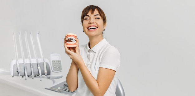 Dentista donna sorridente con mockup di mascelle umane su sfondo bianco banner per il concetto di tema dentale