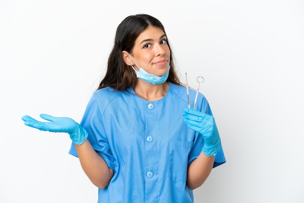 Dentista donna tenendo gli strumenti su sfondo bianco isolato avendo dubbi mentre alzando le mani