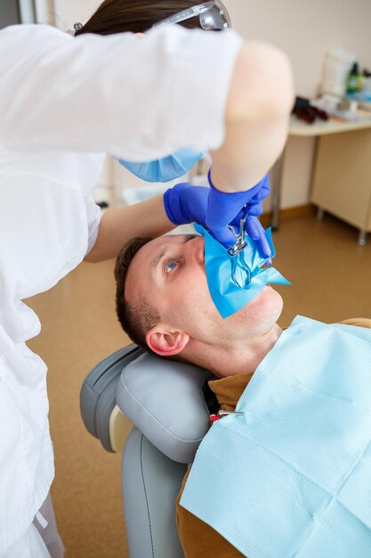 Dentista durante il trattamento di un paziente di sesso maschile. Dentista femminile in maschera facciale con paziente di sesso maschile seduto sulla sedia del dentista seduto in clinica odontoiatrica. Messa a fuoco selettiva