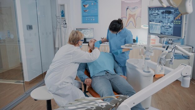 Dentista e assistente che consultano gli strumenti dentali dopo l'intervento chirurgico per controllare il lavoro della dentatura nell'armadietto di stomatologia. Squadra di odontoiatria che esamina i denti per vedere la procedura chirurgica finita.