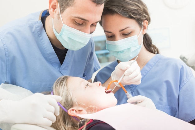 Dentista e assistente dentario che esaminano i denti della ragazza