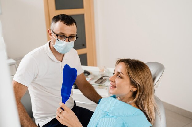 Dentista e donna paziente in odontoiatria Consultazione con il dentista in odontoiatria Trattamento dei denti Ragazza che si guarda allo specchio dal dentista Paziente felice di odontoiatria