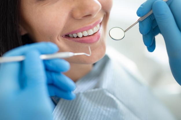 Dentista esaminando i denti del colpo del primo piano della giovane donna felice