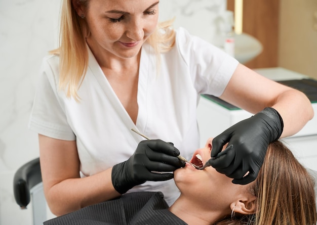 Dentista femminile al lavoro con il paziente che esamina i suoi denti con strumenti dentali