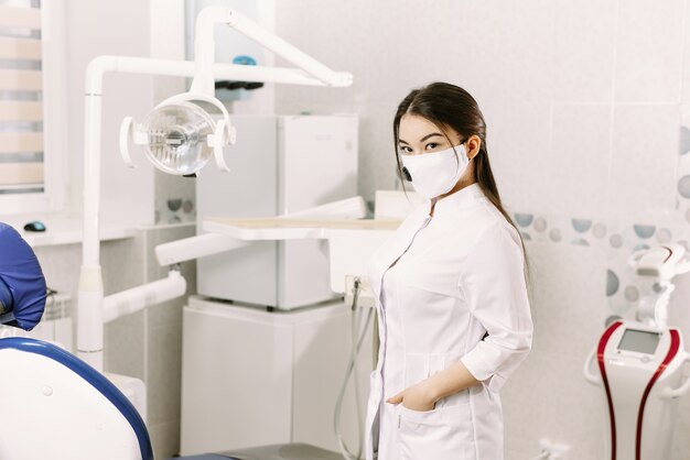 Dentista femminile allegro che sorride al suo ufficio. Bella studentessa in una maschera protettiva