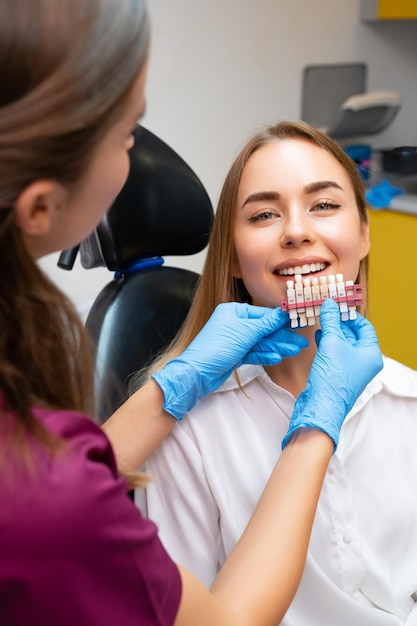 Dentista femminile che abbinano le sfumature dei denti prima della procedura di sbiancamento per il giovane paziente al