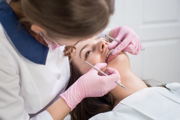 Dentista femminile che controlla i denti pazienti con i ganci del metallo all'ufficio della clinica dentale