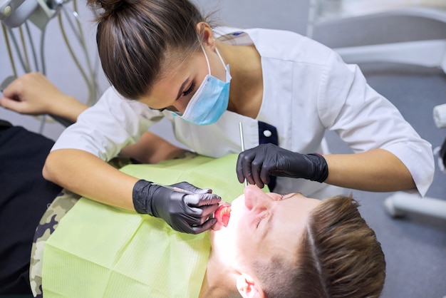 Dentista femminile che cura i denti al paziente, giovane in sedia alla clinica dentale.