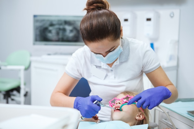 Dentista femminile che cura i denti di un bambino paziente nella sua clinica