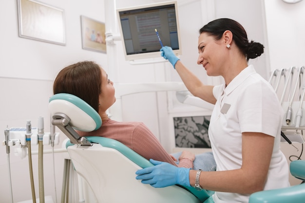 Dentista femminile che istruisce il suo paziente, lavorando presso la sua clinica odontoiatrica