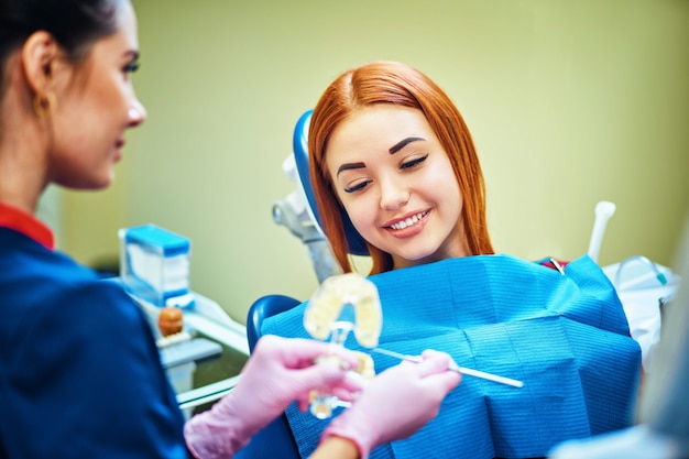 Dentista femminile che mostra la mascella artificiale del paziente presso lo studio dentistico