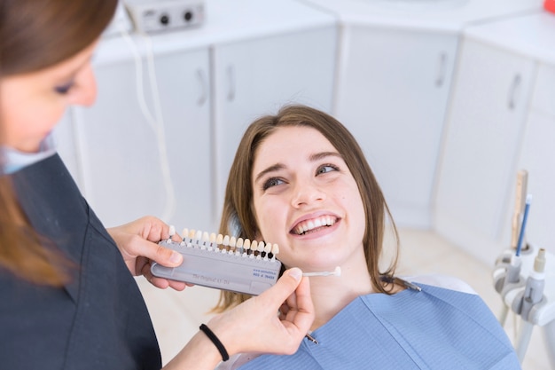 Dentista femminile con i campioni di colore del dente che scelgono l&#39;ombra per il paziente femminile