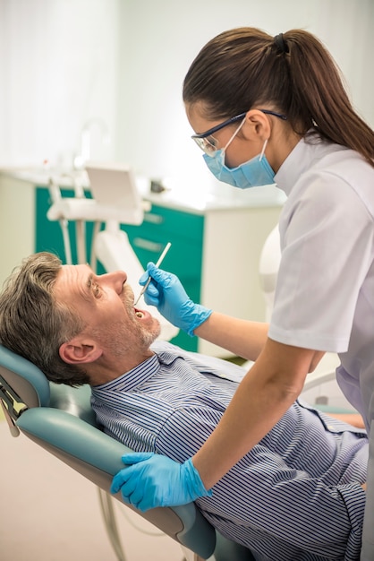 Dentista femminile con il suo cliente senior che esamina un paziente.