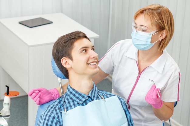 Dentista femminile e giovane nell'ufficio del dentista. Il giovane bello sta facendo il controllo dentale nello studio dentistico