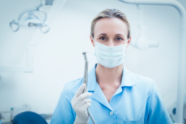 Dentista femminile in maschera chirurgica che tiene strumento dentale