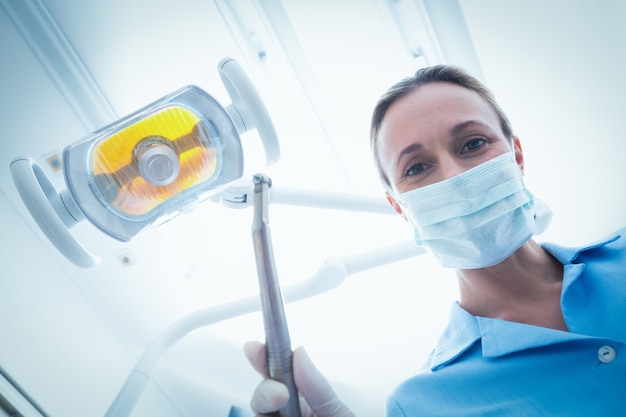 Dentista femminile in maschera chirurgica che tiene strumento dentale