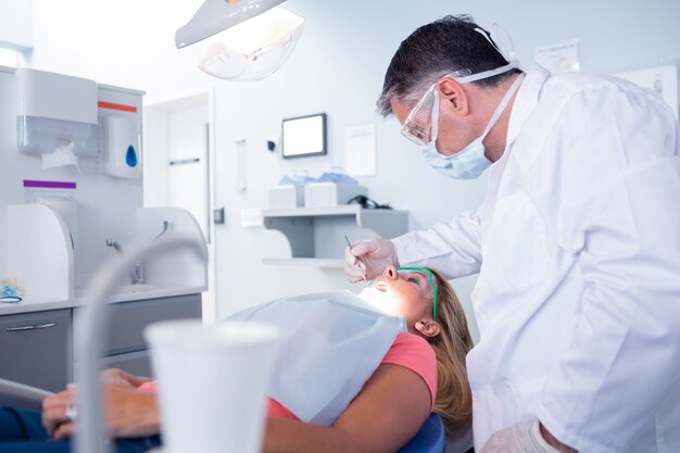 Dentista in mascherina chirurgica che esamina i denti dei pazienti