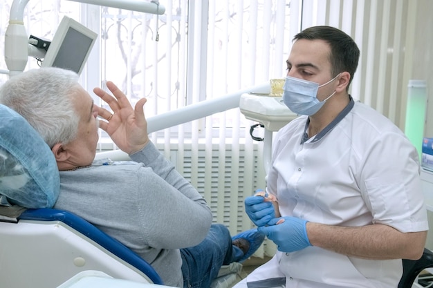Dentista maschio che consulta il paziente anziano prima del trattamento nella clinica odontoiatrica