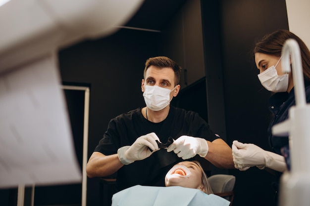 Dentista maschio in studio dentistico che parla con una paziente e la prepara per il trattamento Spiegando la procedura di nuovi impianti dentaliVista posteriore del focus del paziente su un dentista